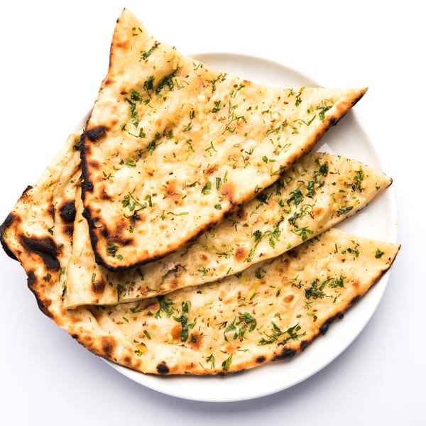 Three pieces of golden-brown garlic naan bread, garnished with green herbs, on a white plate.