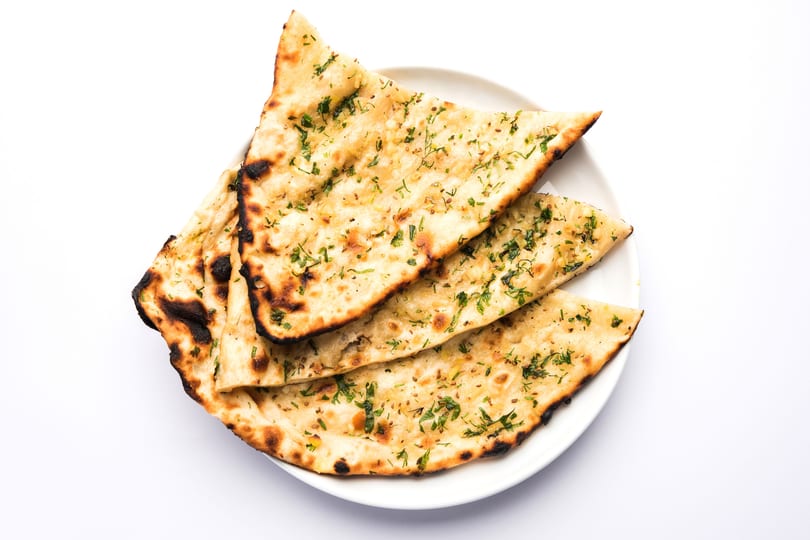 Three pieces of golden-brown garlic naan bread, garnished with green herbs, on a white plate.