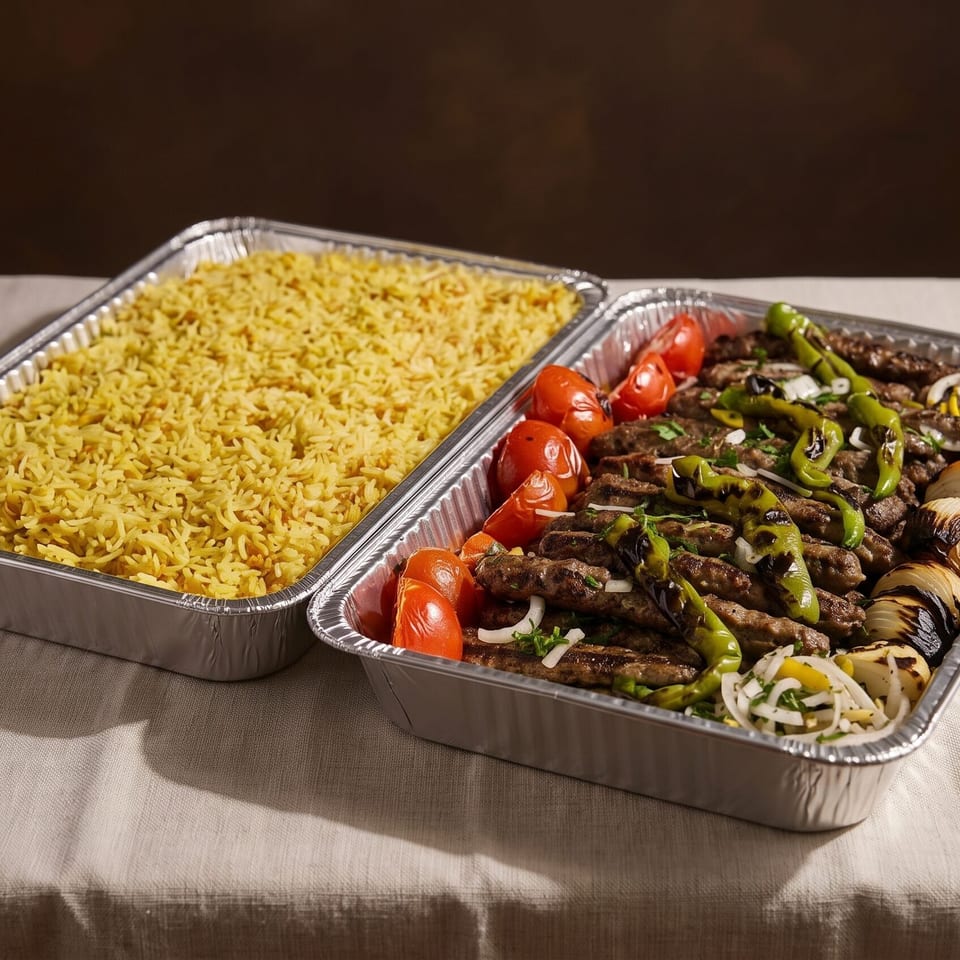 Two catering trays of food, one with yellow rice and the other with grilled meat, vegetables.