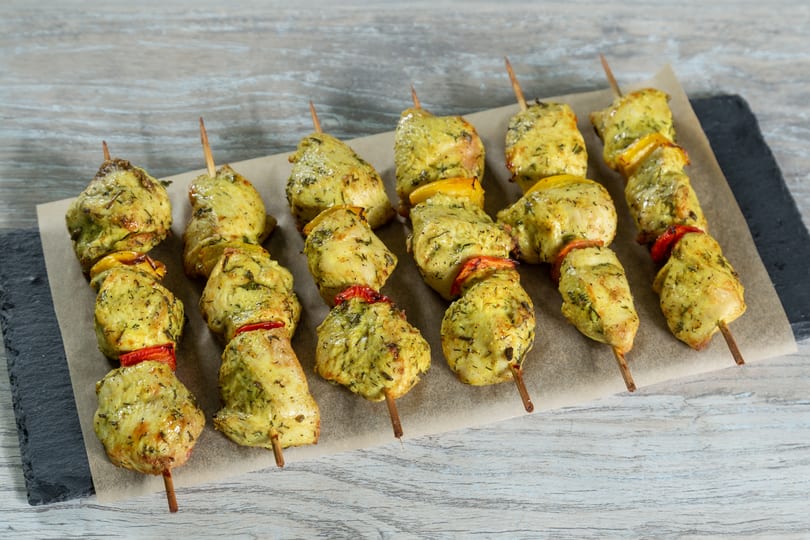 Chicken skewers with yellow and red bell peppers on parchment paper and a slate board.