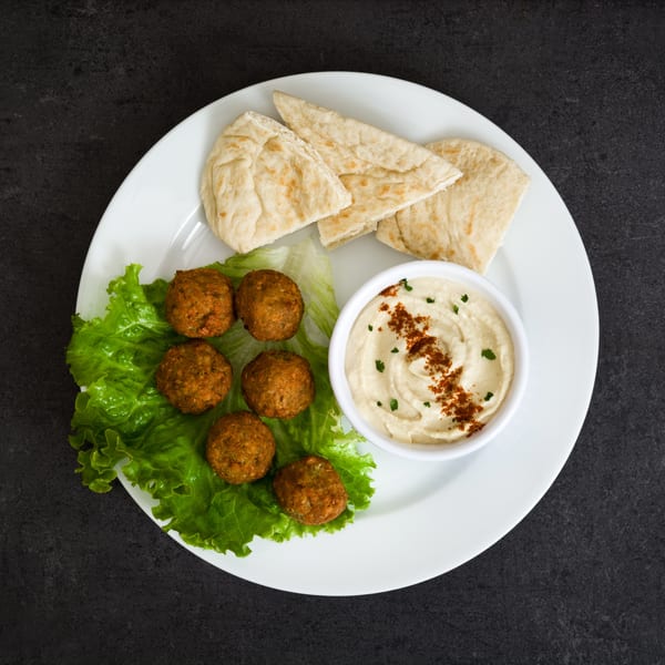 Falafel balls on lettuce with hummus and pita bread on a white plate.