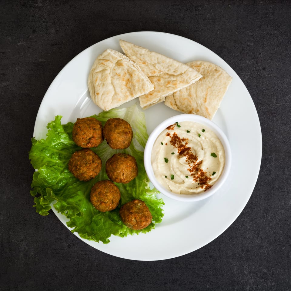 Falafel balls on lettuce with hummus and pita bread on a white plate.