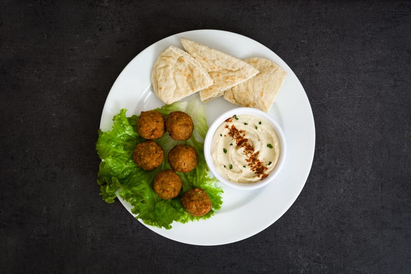 Falafel balls on lettuce with hummus and pita bread on a white plate.