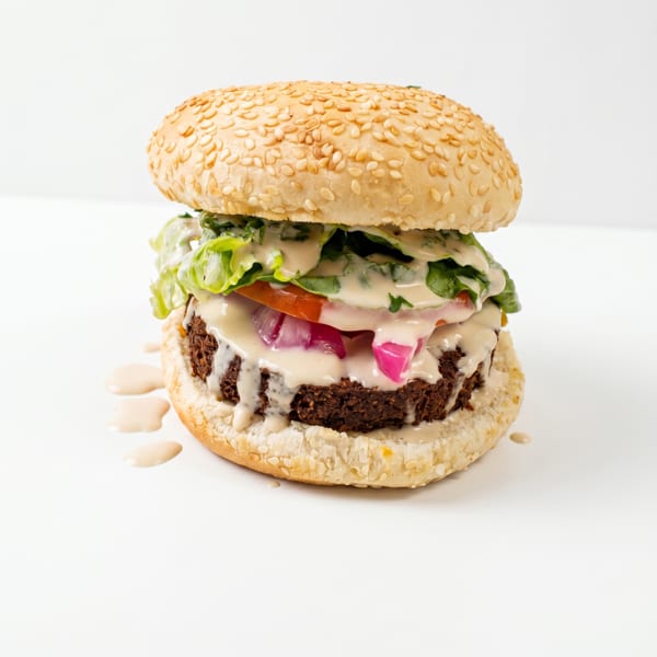 A falafel burger on a sesame seed bun with lettuce, tomato, red onion, and tahini sauce.