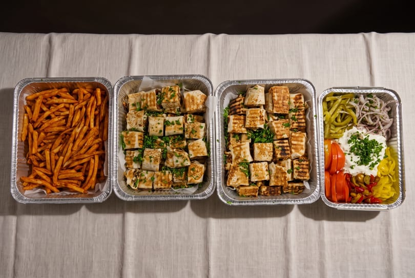 Four foil trays of food, including french fries, cut wraps, and a salad with various toppings.